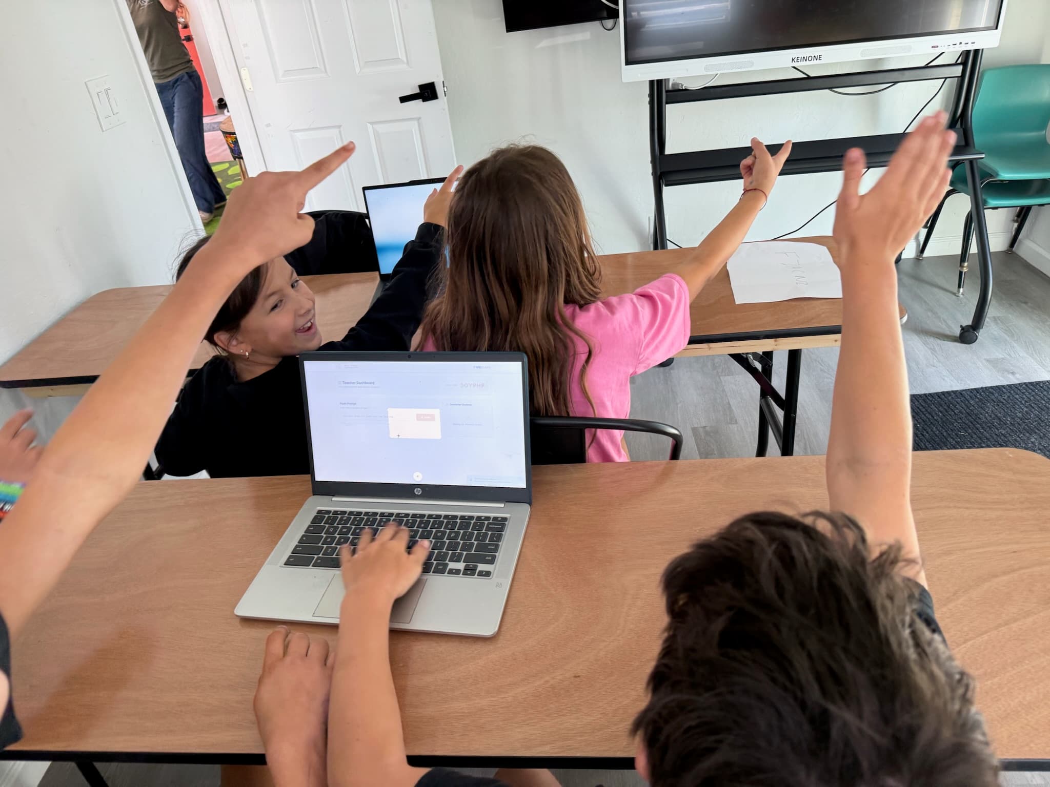 Students raising their hands around a laptop during a lesson